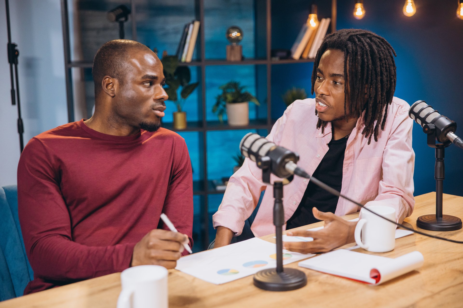 Two African American podcasters recording a new episode in their studio, discussing business strategies and analyzing charts