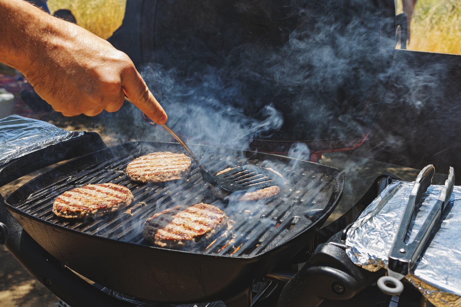 Beef patties on the grill close-up, man cooking burgers outdoors