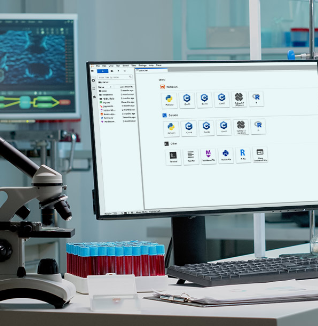 A laboratory bench with scientific equipment including a microscope, pipettes, glassware, racks of test tubes, and a computer monitor displaying scientific software in a well-lit research lab.