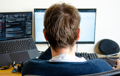 man-is-holding-phone-in-hand-wireless-trading-con-2025-03-10-00-26-45-utc-2 | Iterators Person viewed from behind working on multiple computer monitors, focused on coding and emails.