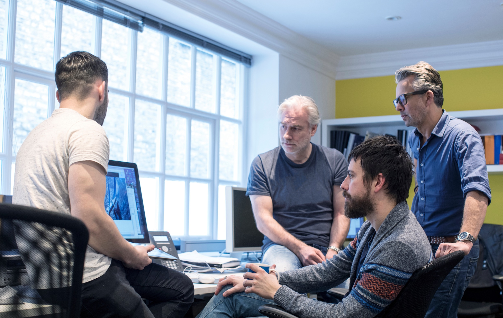 three-computer-screens-with-computer-programming-c-2024-11-01-02-32-31-utc-2 | Iterators Four people having a discussion around a computer screen in a bright office setting.