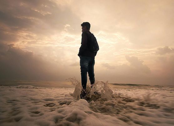 a photo of a man standing on a beach with waves along his feet