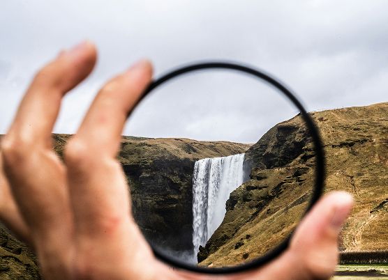 photo of hand holding a circle that frames a waterfall