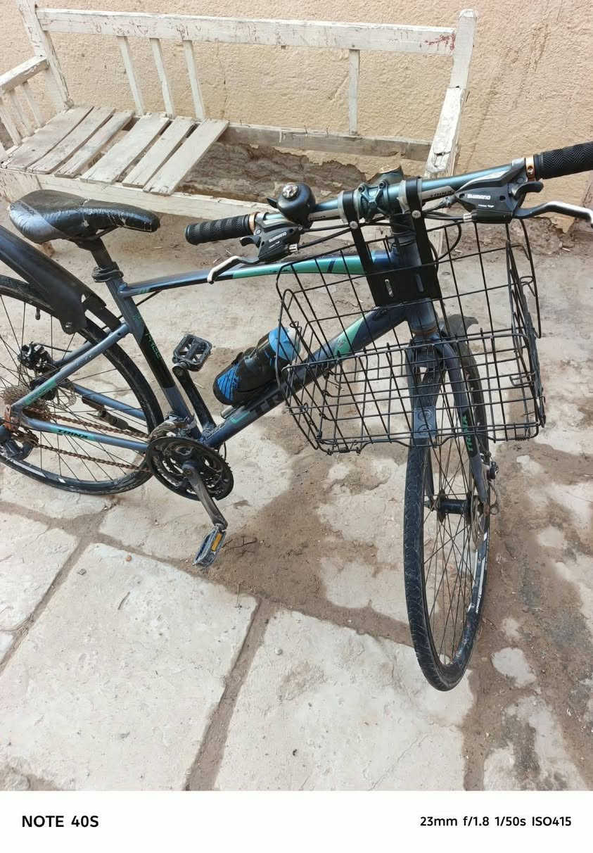 Hybrid / City Bike) من شركة ترينكس (Trinx).  
​أبرز المواصفات والتفاصيل الظاهرة في الصورة:
​العلامة التجارية: Trinx (مكتوبة بوضوح على الهيكل/الإطار الأسفل).  
​الفئة (Type): دراجة هجينة (تجمع بين دراجات الطرق ودراجات الجبال)، حيث تأتي بإطارات رفيعة ونسبة انسيابية عالية تناسب الطرق المعبدة والأسفلت، مع هيكل مريح للقيادة اليومية داخل المدينة.  
​نظام التروس (المغيرات): تعتمد على مغيرات سرعة من شركة Shimano (مكتوب على المقود) مع نظام ناقل حركة خلفي (Derailleur) متدرج السرعات.  
​نظام الفرامل: فرامل قرصية (Disc Brakes) سلكية (ميكانيكية) على العجلات لزيادة قوة وقوف الدراجة.  
​الإكسسوارات المضافة:
​سلة أمتعة أمامية شبكية.  
​جاملغ (مصد طين/ماء) خلفي بلاستيكي.  
​حاملة قنينة ماء مع مطارة رياضة.  
​جرس تنبيه يدوي على المقود.  
السعر 175 الف

نص مكتوب في الصور:
- NOTE 40S 23mm f/1.8 1/50s ISO395
- NOTE 40S 23mm f/1.8 1/50s ISO347
- NOTE 40S 23mm f/1.8 1/50s ISO403
- NOTE 40S 23mm f/1.8 1/50s ISO415
