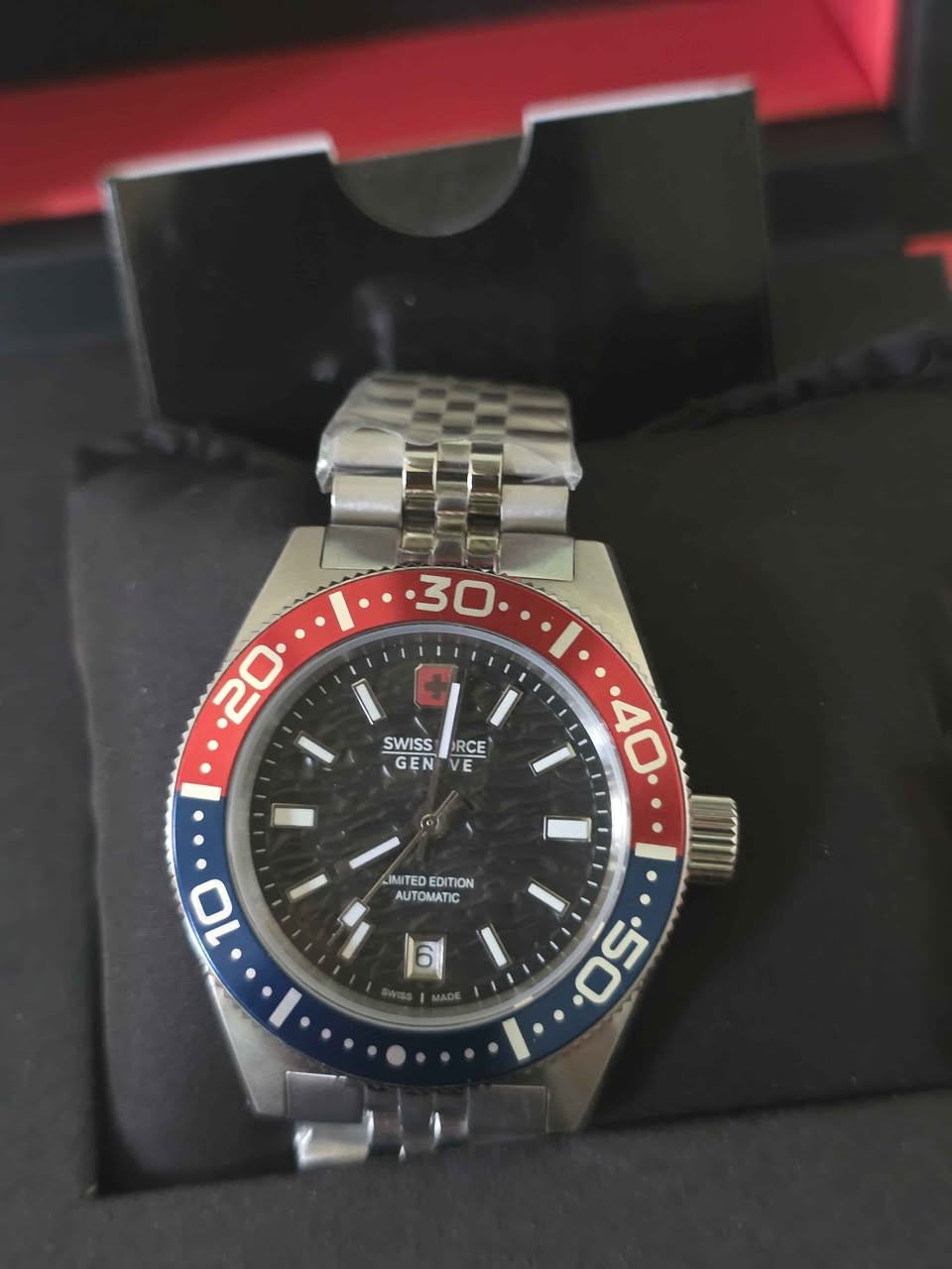 Swiss Force Genève (إصدار محدود / Limited Edition)، وتحمل موديل رقم SF.D812S.01.تأتي الساعة بتصميم رياضي فاخر مستوحى من ساعات الغوص الشهيرة (طراز البيبسي) وتتميز بالصفات والمواصفات التالية:نظام الحركة: ميكانيكية أوتوماتيكية (Automatic) تعتمد على حركة المعصم لتشغيلها، وتوفر مخزون طاقة يدوم لفترة طويلة.الصناعة والمنشأ: سويسرية بالكامل (Swiss Made).المينا (وجه الساعة): لون أسود ذو ملمس كربوني بارز مع عقارب ومؤشرات مضيئة تدعم الرؤية الليلية.الإطار الخارجي (Bezel): إطار دوار بلونين (أزرق وأحمر) لقياس الوقت.السوار (السير): مصنوع من الستانلس ستيل (الفولاذ المقاوم للصدأ) عالي الجودة بتصميم خماسي الحلقات (Jubilee).الزجاج: كريستال معدني مطلي بطبقة زفير مقاومة للخدوش والصدمات لضمان المتانة والوضوح.أبعاد الهيكل: القطر 40 ملم، وهو مقاس مثالي ومريح للمعصم.الميزات الإضافية: نافذة لعرض التاريخ 
عند مؤشر الساعة 6 ومقاومة للماء حتى 5 بار (50 متراً)

*********** بغداد, العراق
