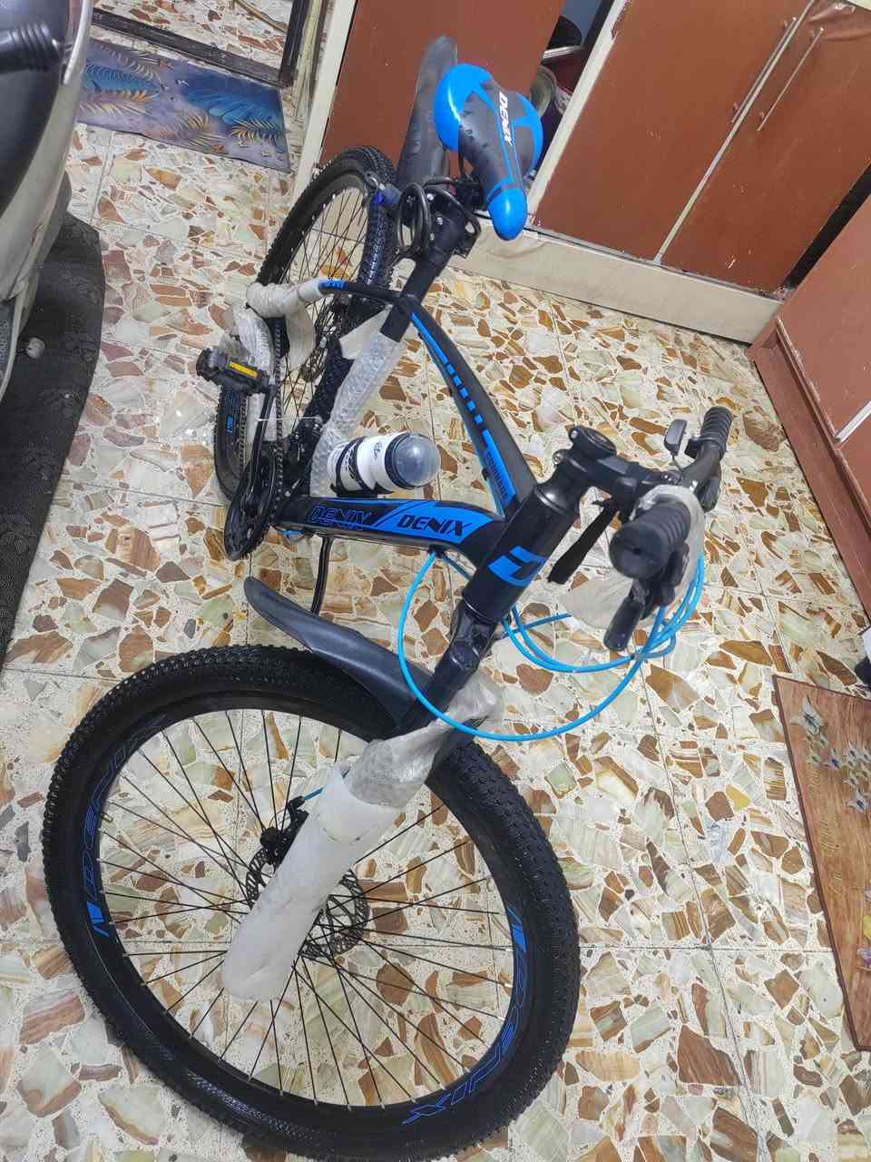 سلام عليكم بايسكل DENIX جبلي - للبيع 🚴‍♂️
​المواصفات والتفاصيل:
​الماركة: DENIX (أصلي).
​النوع: جبلي (Mountain Bike) مناسب للمشي اليومي وللطرق الوعرة.
​الحالة: جديد (مغلف بتغليف الشركة).
​اللون: أسود مع تطعيم أزرق مميز.
​نظام المكابح: ديسك (Disc Brakes) أمامي وخلفي لثبات وقوة توقف.
​المساعدات: دبل أمامي امتصاص صدمات لتنعيم القيادة.
​السرعات: نظام جيرات/دوشج متعدد السرعات تحكم كامل.
​الملحقات المرفقة:
​مطارة ماء مع القاعدة.
​قماريات (قاطعات طين) أمامي وخلفي.
​جك (ستاند) جانبي.
​كمر (سرج) رياضي مريح DENIX.
​📍 المكان: بغداد مدينه الصدر 
📞 للتواصل:  *********** 
💰 السعر:  190
