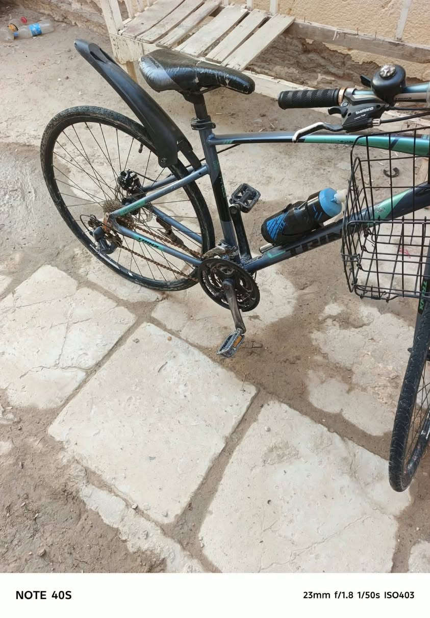 Hybrid / City Bike) من شركة ترينكس (Trinx).  
​أبرز المواصفات والتفاصيل الظاهرة في الصورة:
​العلامة التجارية: Trinx (مكتوبة بوضوح على الهيكل/الإطار الأسفل).  
​الفئة (Type): دراجة هجينة (تجمع بين دراجات الطرق ودراجات الجبال)، حيث تأتي بإطارات رفيعة ونسبة انسيابية عالية تناسب الطرق المعبدة والأسفلت، مع هيكل مريح للقيادة اليومية داخل المدينة.  
​نظام التروس (المغيرات): تعتمد على مغيرات سرعة من شركة Shimano (مكتوب على المقود) مع نظام ناقل حركة خلفي (Derailleur) متدرج السرعات.  
​نظام الفرامل: فرامل قرصية (Disc Brakes) سلكية (ميكانيكية) على العجلات لزيادة قوة وقوف الدراجة.  
​الإكسسوارات المضافة:
​سلة أمتعة أمامية شبكية.  
​جاملغ (مصد طين/ماء) خلفي بلاستيكي.  
​حاملة قنينة ماء مع مطارة رياضة.  
​جرس تنبيه يدوي على المقود.  
السعر 175 الف

نص مكتوب في الصور:
- NOTE 40S 23mm f/1.8 1/50s ISO395
- NOTE 40S 23mm f/1.8 1/50s ISO347
- NOTE 40S 23mm f/1.8 1/50s ISO403
- NOTE 40S 23mm f/1.8 1/50s ISO415