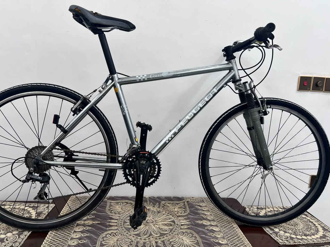 للبيع دراجة هوائية بيجو (Peugeot).  
​الموديل: كولين (Colline).  
​نوع الدراجة: دراجة هجين / جبلية للمدينة (Hybrid / City Trekking Bike).  
​حجم العجلات (التاير): قياس 28 إينش (700c).  
​حجم الهيكل (الفريم): 26 قياس متوسط/كبير (M/L - تقريباً 18 إلى 20 إينش/48-52 سم) من الألمنيوم المصقول الخفيف.  
​ناقل الحركة (الجير):
​ناقل خلفي: Shimano Acera.  
​محول السرعات (الشيفتر): Shimano RevoShift (قبضات تدوير باليد).  
​عدد السرعات: 21 سرعة (3 تروس أماما x 7 تروس خلفاً). قطعة كلش نظيفة وقوية بالاستخدام السعر 120وبي مجال بسيط مكاني بغداد تلفون ***********
