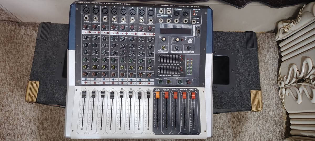 هذا الجهاز هو مكسر صوت مدمج بمكبر صوت (Powered Audio Mixer) أو ما يُعرف بـ جهاز دمج وتكبير الصوت. يُستخدم لاستقبال الإشارات الصوتية من عدة مصادر، تعديلها، وتكبيرها لبثها عبر السماعات.
المكونات الوظيفية الرئيسية:
 * قنوات الإدخال (1 - 8): تحتوي على منافذ XLR والمقابس (6.35mm) لتوصيل الميكروفونات والآلات الموسيقية، مع مفاتيح للتحكم بالصوت (EQ: High, Mid, Low)، والتأثيرات (FX)، ومستوى الصوت (Faders).
 * معادل الصوت البياني (Graphic Equalizer): مكوّن من 7 نطاقات ترددية لتعديل درجة جودة الصوت وإزالة الترددات المزعجة (الفيذباك).
 * مؤثرات رقمية (DSP / FX Parameter): يوفر مؤثرات صوتية جاهزة مثل الصدى (Echo/Reverb) للغناء أو الحديث.
 * مشغل ميديا مدمج: يدعم التوصيل عبر البلوتوث (Bluetooth) ومنافذ USB و SD Card لتشغيل الملفات الصوتية مباشرة.
 * مفاتيح التحكم الرئيسية (Master Output): منزلقات باللون البرتقالي/الأحمر للتحكم في مستوى الصوت النهائي الموجه للسماعات الرئيسية (MAIN L/R) وللمشغل المدمج (MP3).
 * طاقة وهمية (Phantom Power +48V): ميزة لتشغيل ميكروفونات المكثف (Condenser Mics).
الاستخدامات الشائعة:
يُستخدم في الحفلات، المناسبات، المساجد، قاعات الاجتماعات، أو مع أجهزة الصوت المنزلية والتسجيل البسيط.

السلام عليكم هذا الجهاز للبيع مع عدد سماعات 2 جهاز شبه جديد
للإستفسار الإتصال على الرقم ***********

