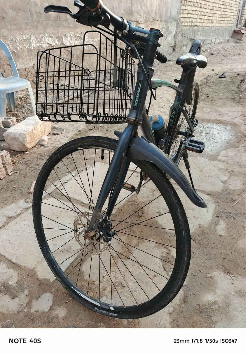 Hybrid / City Bike) من شركة ترينكس (Trinx).  
​أبرز المواصفات والتفاصيل الظاهرة في الصورة:
​العلامة التجارية: Trinx (مكتوبة بوضوح على الهيكل/الإطار الأسفل).  
​الفئة (Type): دراجة هجينة (تجمع بين دراجات الطرق ودراجات الجبال)، حيث تأتي بإطارات رفيعة ونسبة انسيابية عالية تناسب الطرق المعبدة والأسفلت، مع هيكل مريح للقيادة اليومية داخل المدينة.  
​نظام التروس (المغيرات): تعتمد على مغيرات سرعة من شركة Shimano (مكتوب على المقود) مع نظام ناقل حركة خلفي (Derailleur) متدرج السرعات.  
​نظام الفرامل: فرامل قرصية (Disc Brakes) سلكية (ميكانيكية) على العجلات لزيادة قوة وقوف الدراجة.  
​الإكسسوارات المضافة:
​سلة أمتعة أمامية شبكية.  
​جاملغ (مصد طين/ماء) خلفي بلاستيكي.  
​حاملة قنينة ماء مع مطارة رياضة.  
​جرس تنبيه يدوي على المقود.  
السعر 175 الف

نص مكتوب في الصور:
- NOTE 40S 23mm f/1.8 1/50s ISO395
- NOTE 40S 23mm f/1.8 1/50s ISO347
- NOTE 40S 23mm f/1.8 1/50s ISO403
- NOTE 40S 23mm f/1.8 1/50s ISO415
