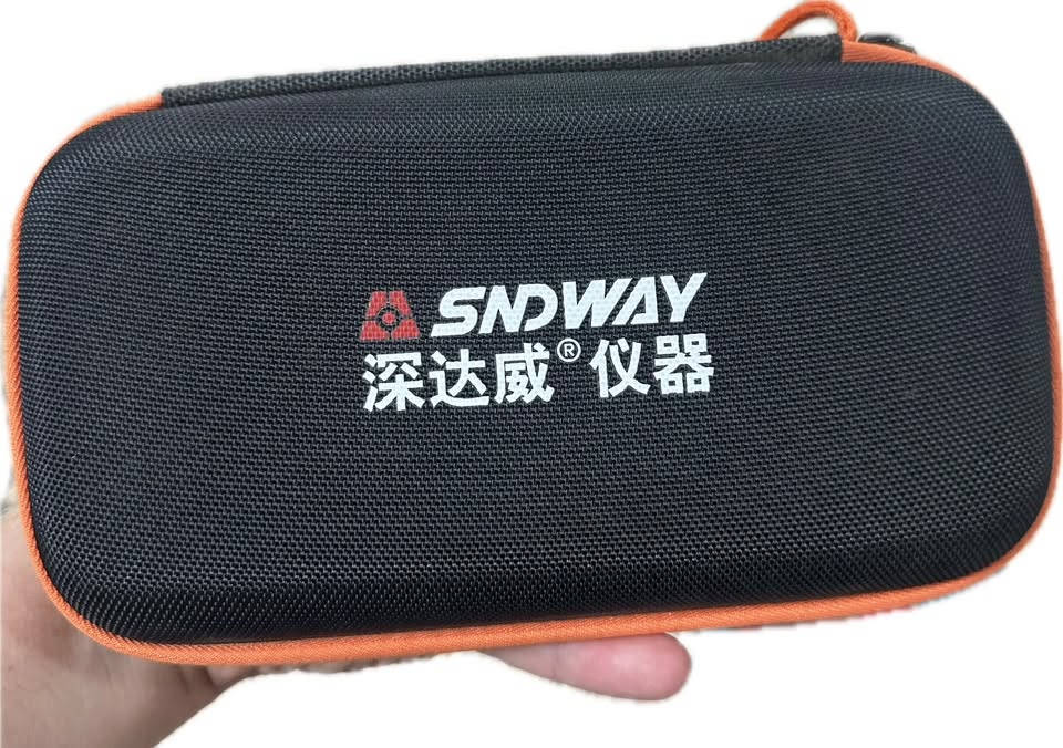 تُظهر الصورة جهاز كشف تسريب غازات الهالوجين (Halogen Detector) من ماركة SNDWAY، طراز SW-743A، موضوعاً داخل حقيبة حفظ واقية.  
إليك تفاصيل الجهاز الظاهر في الصورة:
 نوع الجهاز: كاشف تسريب غازات الهالوجين (يُستخدم عادة في فحص تسريب غازات التكييف والتبريد).  
 الماركة والطراز: SNDWAY SW-743A.  
 التصميم والمكونات: يحتوي الجهاز على شاشة عرض رقمية، وأزرار للتحكم (زر الطاقة، زر الرجوع، زر الإدخال، أزرار الأسهم، وزر الإنذار ALARM).  
 المسبار: يتميز بعنق مرن طويل ينتهي بمستشعر للوصول إلى الأماكن الضيقة وصعبة الوصول لفحص التسريب بدقة.  
 حقيبة الحفظ: يأتي الجهاز داخل حقيبة حمل سوداء ذات سحاب وإطار برتقالي اللون تحتوي على جيب شبكي داخلي.
للتواصل واتساب ***********

