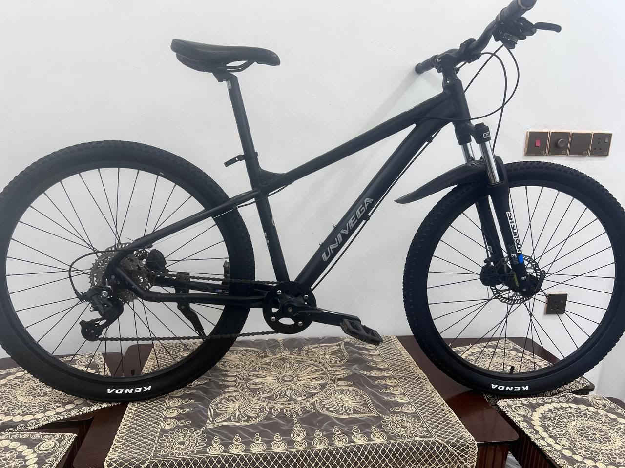 دراجة جبلية ماركة: Univega (علامة تجارية أمريكية أصلية عريقة).  
​الفئة: دراجة جبلية / هجين (Mountain / Trail Bike) مخصصة للطرق الوعرة واليومية.    
الحجم والقياسات
​قياس الإطارات: بحجم 27.5 إنش أو 29 إنش (إطارات رياضية عريضة ومرتفعة).  
​حجم الهيكل (الفرام): ذو تصميم منحرف للأسفل (Low Standover) بحجم يقع بين S (صغير) و M (وسط)، وهو مناسب جداً لراحة الركوب والنزول للأطوال المتوسطة.  
​3. المواصفات الميكانيكية والقطع
​ناقل الحركة (الجير): محول خلفي من شركة MicroSHIFT المعتمدة مع مسننات خلفية واسعة لتسهيل الصعود.  
​المساعد الأمامي: نظام امتصاص صدمات (جامبين) من شركة SR Suntour.  
​الإطارات (الإطارات الخارجية): من ماركة KENDA عالية الجودة.  
​نظام المكابح: فرامل ديسك (Disc Brakes) توفر استجابة وإيقافاً قوياً.  
​الهيكل: مصنع من الألمنيوم الخفيف والمقاوم للصدأ  السعر 180وبي مجال مكاني بغداد تلفون ***********
