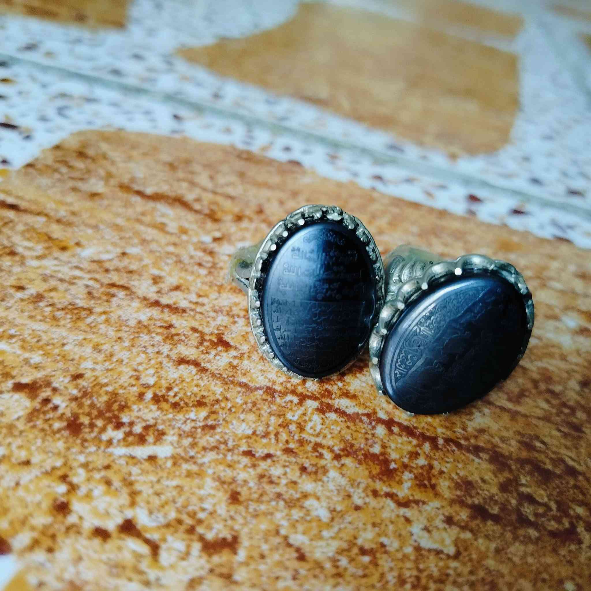هذه المحابس تحتوي على أحجار من نوع الحديد الصيني (Hematite)، وهو نوع شائع ومشهور بنقش النقوش والأدعية والآيات الشريفة:
الخاتم على اليسار:
​منقوش عليه حرز الجلالات السبع، وهو نقش معروف ومأثور يُكتب على فص الحديد الصيني، ويتكون من السطور التالية:
​السطر الأول: أعوذ بجلال الله.
​السطر الثاني: أعوذ بكلمات الله.
​السطر الثالث: أعوذ برسول الله.
​باقي الأسطر: عبارات التوسل والتوكل المتممة للحرز مثل:
​"آمنت بالله وكتبه ورسله"
​"إني واثق بالله ورسله"
​"أشهد أن لا إله إلا الله مخلصاً"
​الخاتم على اليمين:
​يحتوي على نقش دعاء وتوسل بأهل البيت (عليهم السلام) مع أشكال رمزية (مثل كف أبي الفضل العباس أو السيف):
​عبارة "يا علي" أو "يا أبا الفضل العباس" في الجانب.
​أدعية للتحصين والسلامة وطلب الحاجة.
هذه المحابس تحتوي على أحجار من نوع الحديد الصيني (Hematite)، وهو نوع شائع ومشهور بنقش النقوش والأدعية والآيات الشريفة: والسعر خاص.. على هذا الرقم..  
***********
