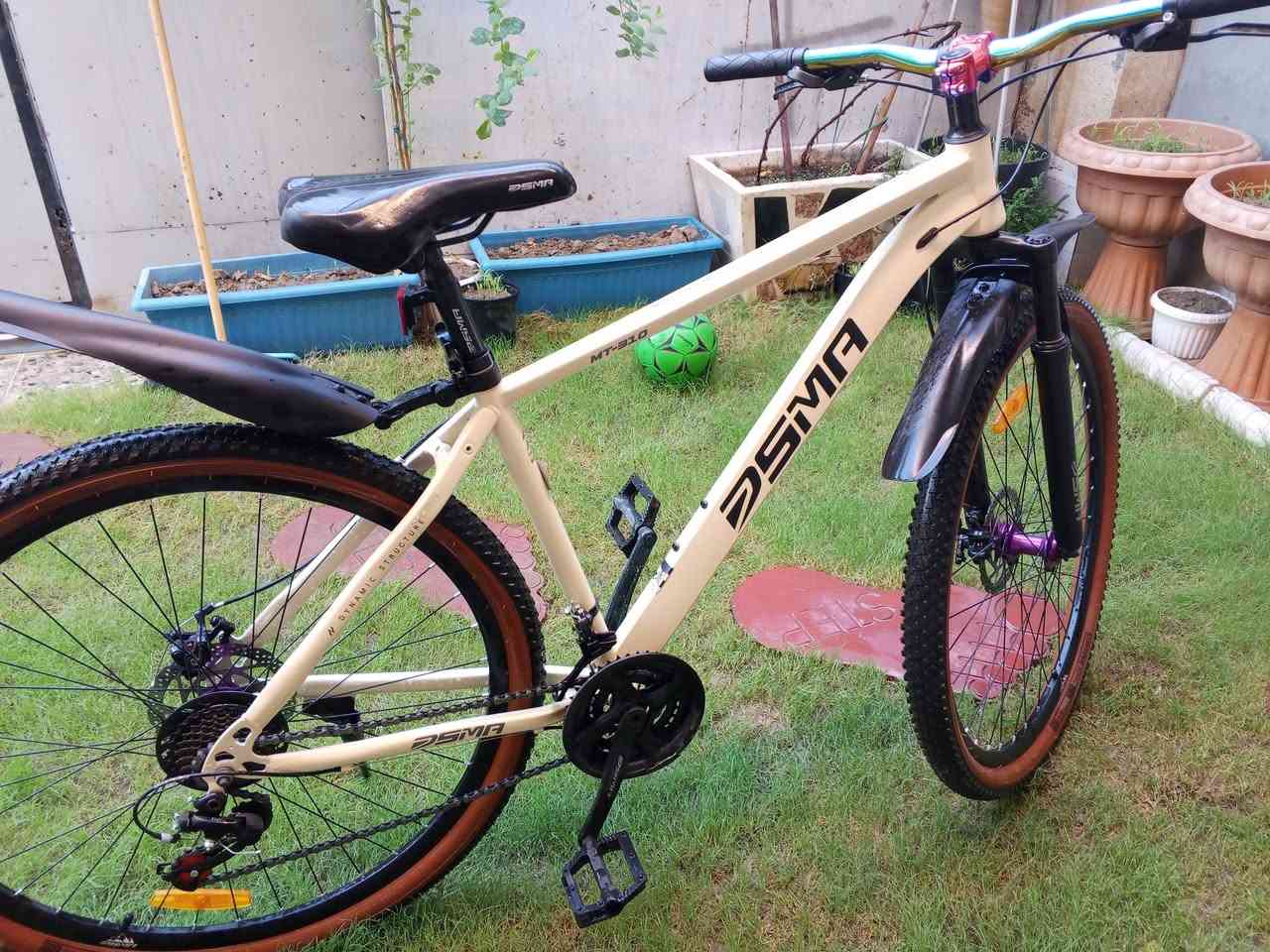 هذا البايسكل من علامة DSMA التجارية، وهي دراجة جبلية (Mountain Bike / MTB) موديل MT-316.
‏المواصفات الفنية الموضحة في الصور:
‏الماركة والموديل: DSMA - موديل MT-316.
‏النوع: دراجة جبلية (Mountain Bike).
‏الهيكل (Frame): ألومنيوم باللون الأوف وايت/البيج، مع تصميم ديناميكي (Dynamic Structure).
‏نظام التروس (السرعات): ناقل حركة (ديلر) خلفي وأمامي تجاري/اقتصادي ماركة HW، بنظام سرعات متعدد (غالباً 21 سرعة: 3 أطباق أمامية × 7 تروس خلفية).
‏المكابح (البريكات): ديسك بريك ميكانيكي (Mechanical Disc Brakes) خلفي وأمامي.
‏المساعدات (Suspension): مساعد أمامي (Front Fork) لامتصاص الصدمات في الطرق الوعرة.
‏الإطارات: إطارات رياضية بحواف بنية (Tan Wall) ومقاس   29 إنش.
‏الملحقات والمميزات الإضافية:
‏
‏مقود (ستيرن) ملون بألوان نيون رياضية (Rainbow/Anodized).
‏ساند جانبي (جك).
‏
‏غير مستعمل 
‏مكاني شهداء البياع 
‏***********
‏
‏سعر 210 وبي مجال 
هذا البايسكل من علامة DSMA التجارية، وهي دراجة جبلية (Mountain Bike / MTB) موديل MT-316.
