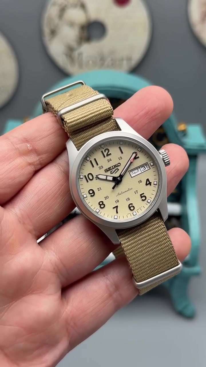 هذه ساعة Seiko 5 Sports Field Watch (الشهيرة بلقب Seiko 5 Desert/Beige Canvas من سلسلة الميدان العسكرية):
المواصفات الفنية
 الماركة والسلسلة: Seiko 5 Sports (سلسلة Field / العسكرية).
 نوع الحركة: أوتوماتيكية (Automatic) بمحرك Caliber 4R36 مع خاصية التعبئة اليدوية وتوقف ثواني التعديل (Hacking).
 المينا (Dial): لون بيج مطفي (Desert Tan / Beige) بتصميم ميداني عسكري كلاسيكي، مع أرقام عربية واضحة للوقت (12 ساعة) وحلقة inner scale بتوقيت 24 ساعة.
 عرض اليوم والتاريخ: نافذة عند الساعة 3 تدعم اللغتين العربية والإنجليزية (ظاهر بالصورة: السبت 31).
 مقاومة الماء: 100 متر (10BAR).
 الهيكل (Case): ستانلس ستيل بإنهاء مطفي غير لامع (Sandblasted / Matte finish) لمظهر عسكري يقلل من الانعكاسات.
 الحزام (Strap): قماش نايلون متين جداً (NATO Style) باللون البيج/الصحراوي المماثل للمينا.
 الزجاج: كريستال Hardlex المقوى.
أبرز المميزات
 تصميم ميداني عسكري (Field Design): يضمن أعلى مستويات وضوح القراءة بفضل الترقيم المزدوج (12/24 ساعة) والعقارب البارزة.
 خفيفة ومريحة: الحزام القماشي العسكري يجعلها خفيفة الوزن على المعصم ومناسبة جداً للاستخدام اليومي الشاق والأجواء الحارة.
 طلاء مضيء (LumiBrite): المؤشرات والعقارب مطلية بمادة مضيئة توفر رؤية ممتازة في الظلام.
 اعتمادية المحرك: محرك 4R36 معروف بطول العمر وسهولة الصيانة ودقة الأداء.

للحجز والاستفسار 
***********

صفحة تكتوك 

https://www.tiktok.com/@harmonytime.iq?_r=1&_t=ZS-99W6WkcffCn
