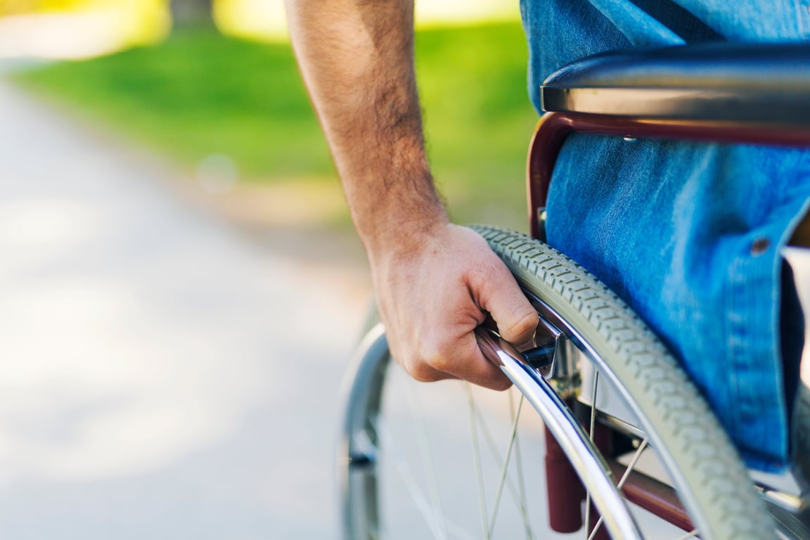 Close up of male hand on wheel of wheelchair during walk in park