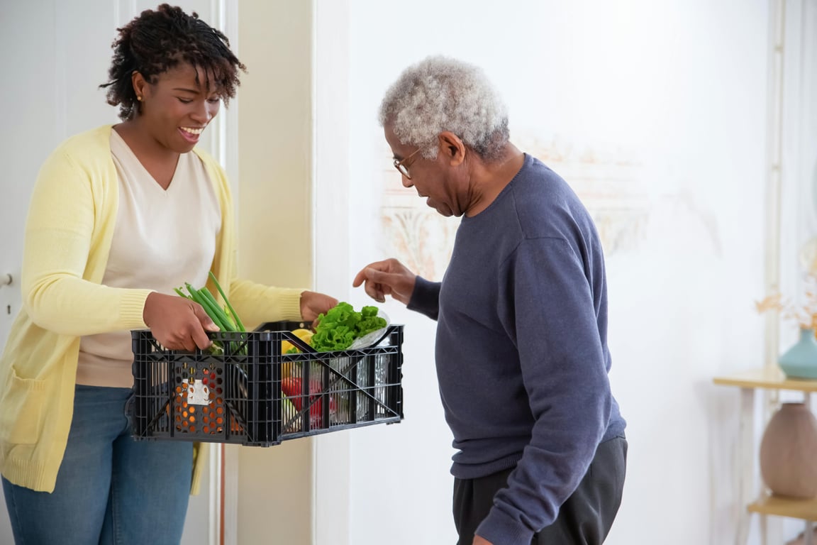 woman bringing groceries to elderly man