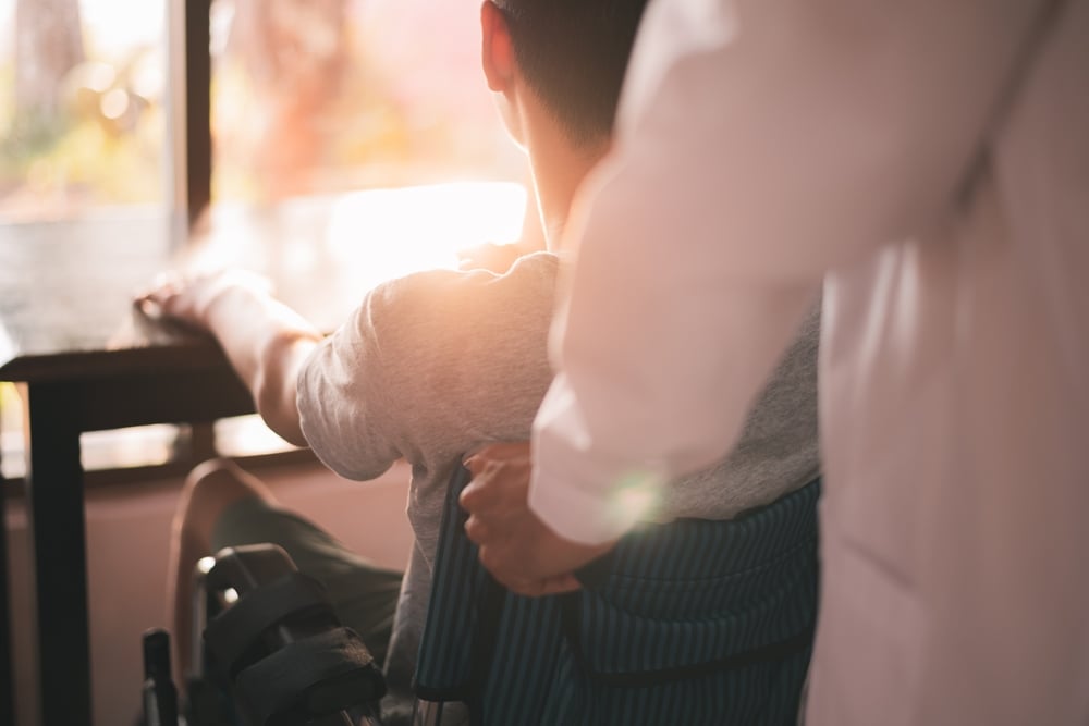 Young man who uses wheelchair brought to desk by health care worker