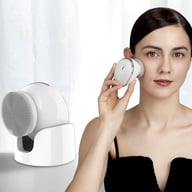 Woman using rechargeable vibrating facial cleansing brush with warm function and charging base