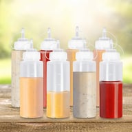 Eight squeeze bottles with visible measurement markings arranged in outdoor kitchen setting