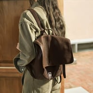 Dark brown leather backpack worn by person showing rear convertible straps