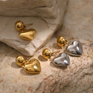 Close-up gold and silver stainless steel heart stud earrings on stone