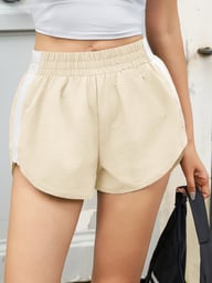 Beige high-waisted dolphin shorts with white stripe, holding a bag