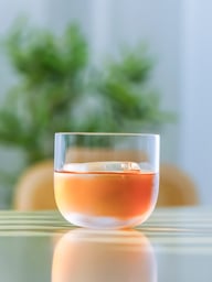 Premium crystal whisky glass with large ice sphere on reflective bar surface