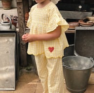 Girl wearing yellow plaid ruffle-sleeve top and pants set outdoors in summer