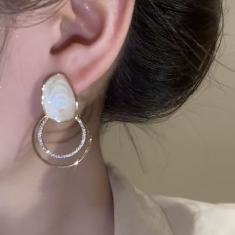 Close-up of sparkly zircon loop earrings showing marbled cream texture and gold plating