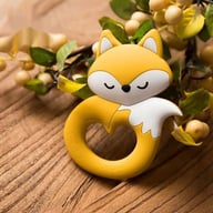 Yellow fox-shaped food-grade silicone baby teether on wooden surface