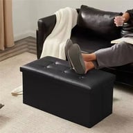 Person sitting on black button-tufted foldable storage ottoman bench