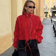 Woman wearing red pleated stand-collar jacket with black pants and sunglasses