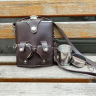 Brown leather flask sleeve with two telescoping cups on wooden bench