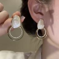Hand holding sparkly geometric loop drop earring next to ear, showing marbled cream resin
