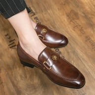 Brown metal-buckle slip-on loafers worn on feet, professional appearance