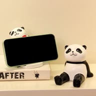 Panda phone holder displaying smartphone on book, cute decorative stand
