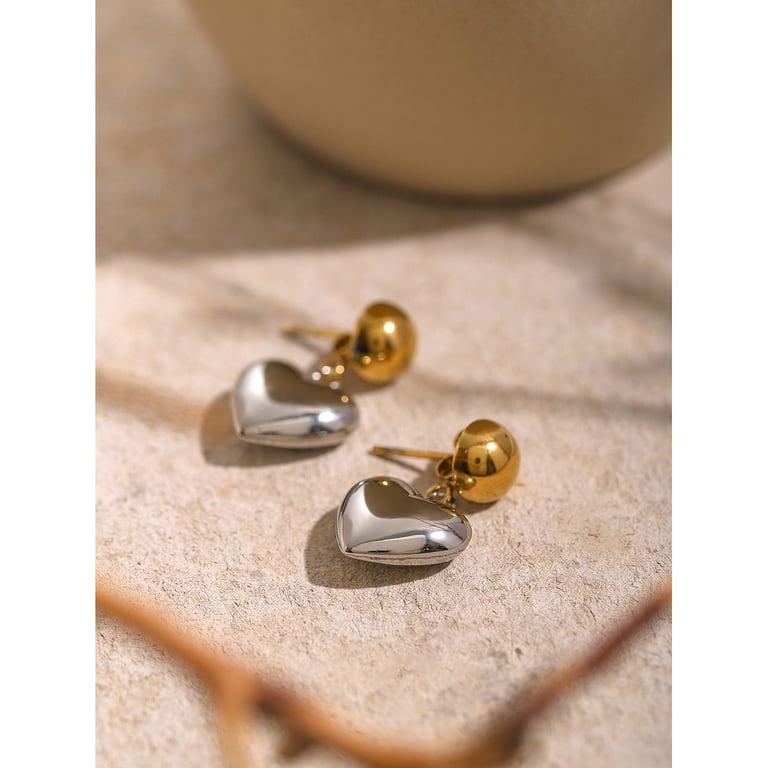 Close-up gold heart earrings on stone with reflective polished finish