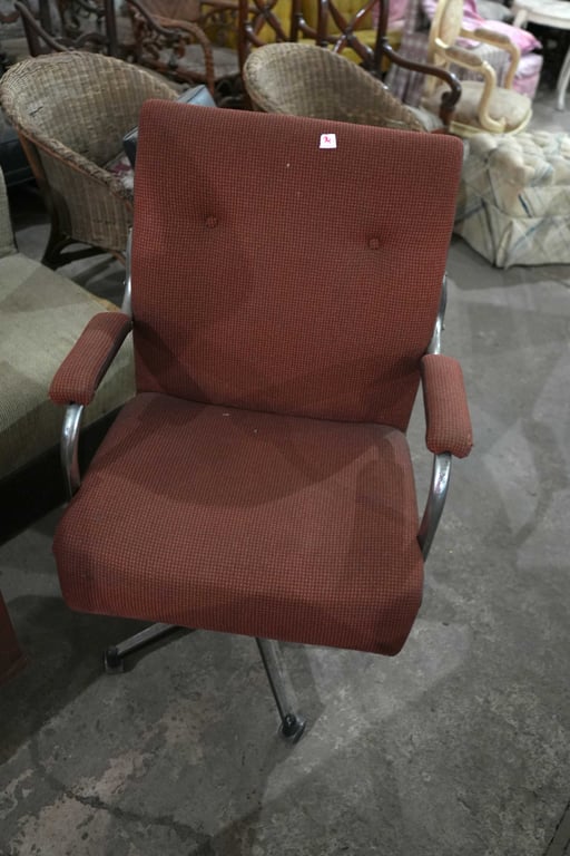 Silla de oficina de hierro y tapizada color naranja oscuro. Con respaldo de brazo y rueditas.