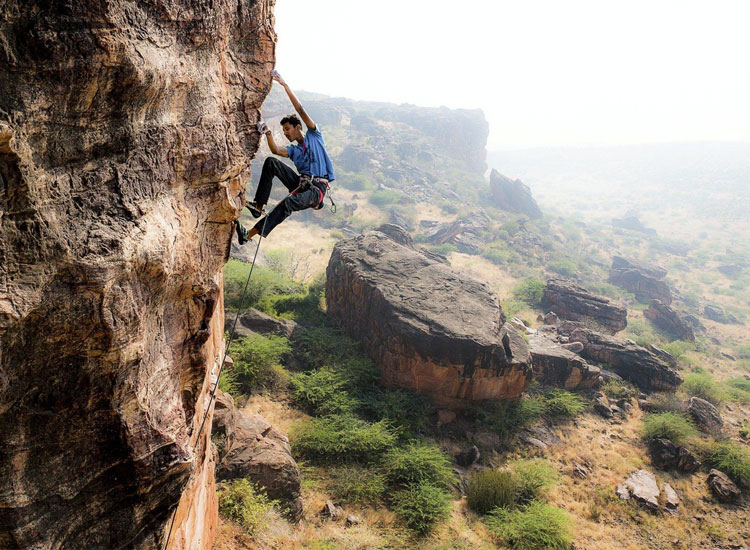 Rock climber scaling the sandstone cliffs of Badami in Karnataka