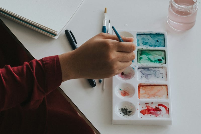 Illustrative image: a hand dipping a paintbrush into a watercolor palette