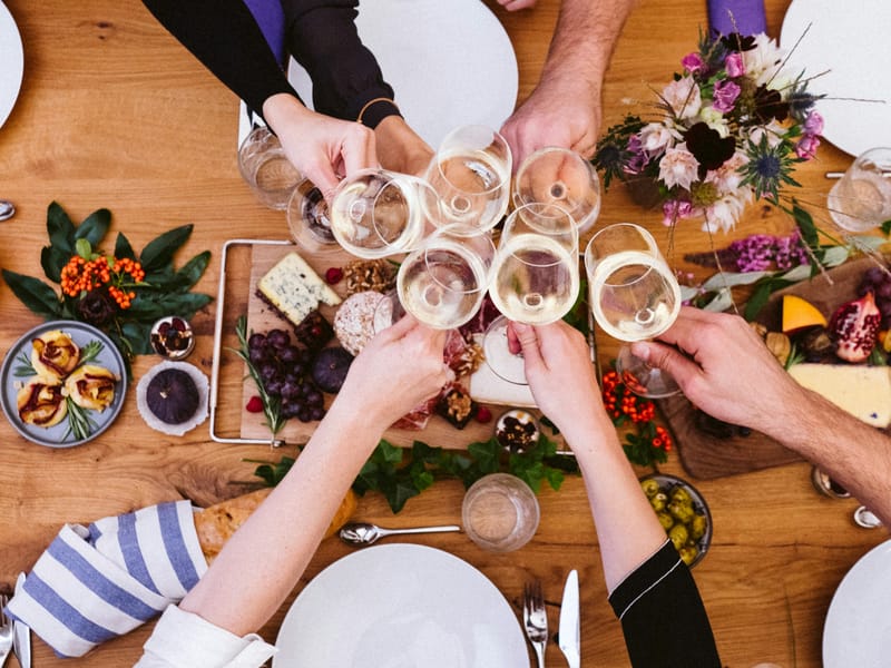 Illustrative image: hands clinking glasses over a shared table spread