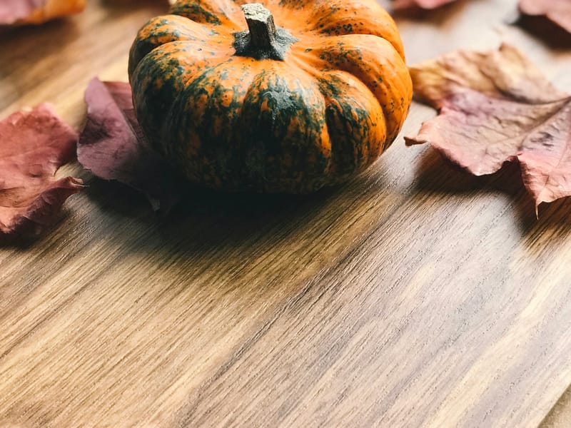 Illustrative image: a pumpkin surrounded by autumn leaves on a wooden table