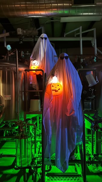Two sheet ghosts holding jack-o'-lantern buckets in the 105 West brewhouse