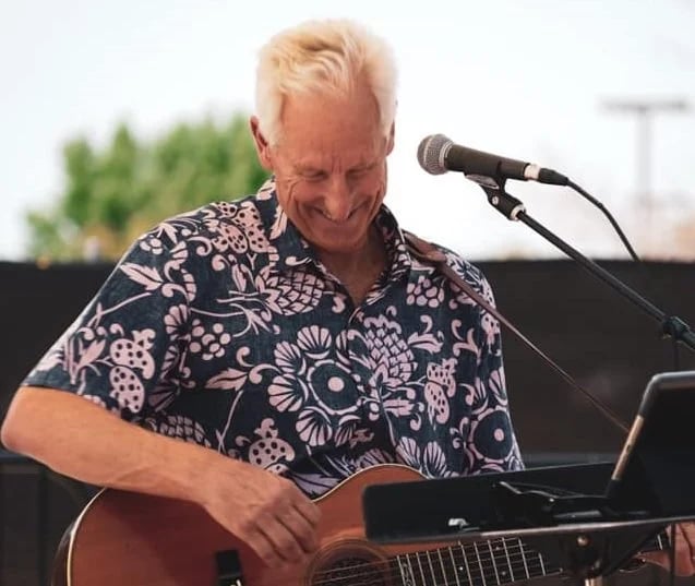 Musician Dave Miller playing acoustic guitar and singing into a microphone