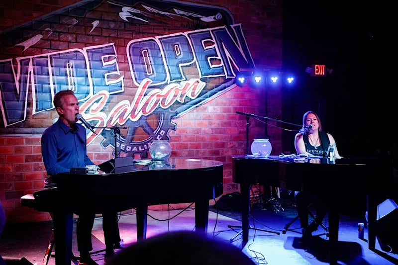 Two dueling pianos performers on stage in front of the Wide Open Saloon sign