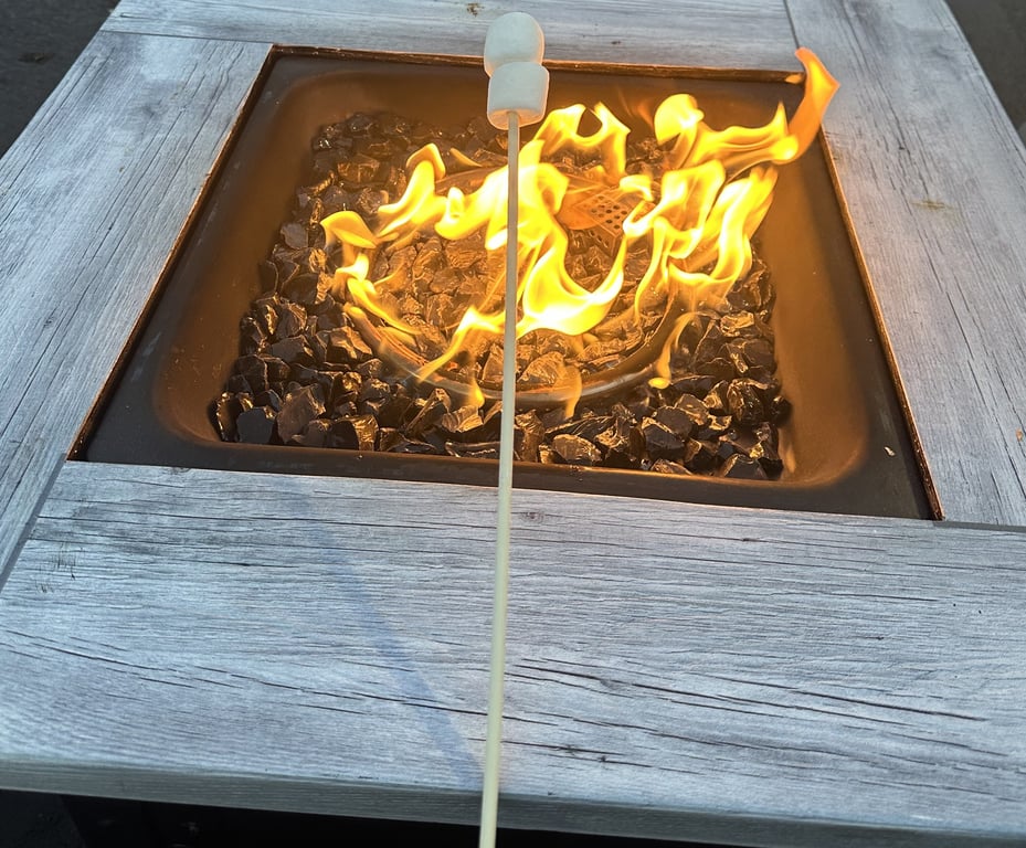 A marshmallow on a roasting stick over the flames of a tabletop fire pit at S'mores Time's setup.