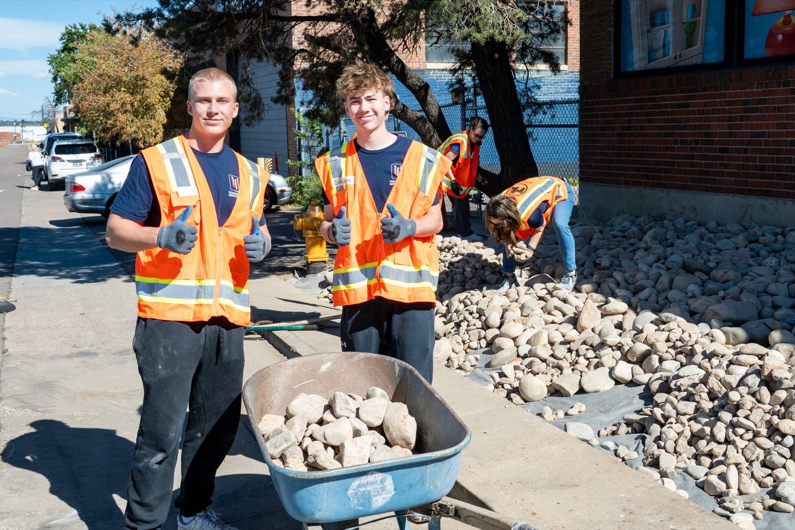 Two YMSL DougCo volunteers push a wheelbarrow of landscape rock toward the entrance of the Habitat for Humanity of Metro Denver ReStore
