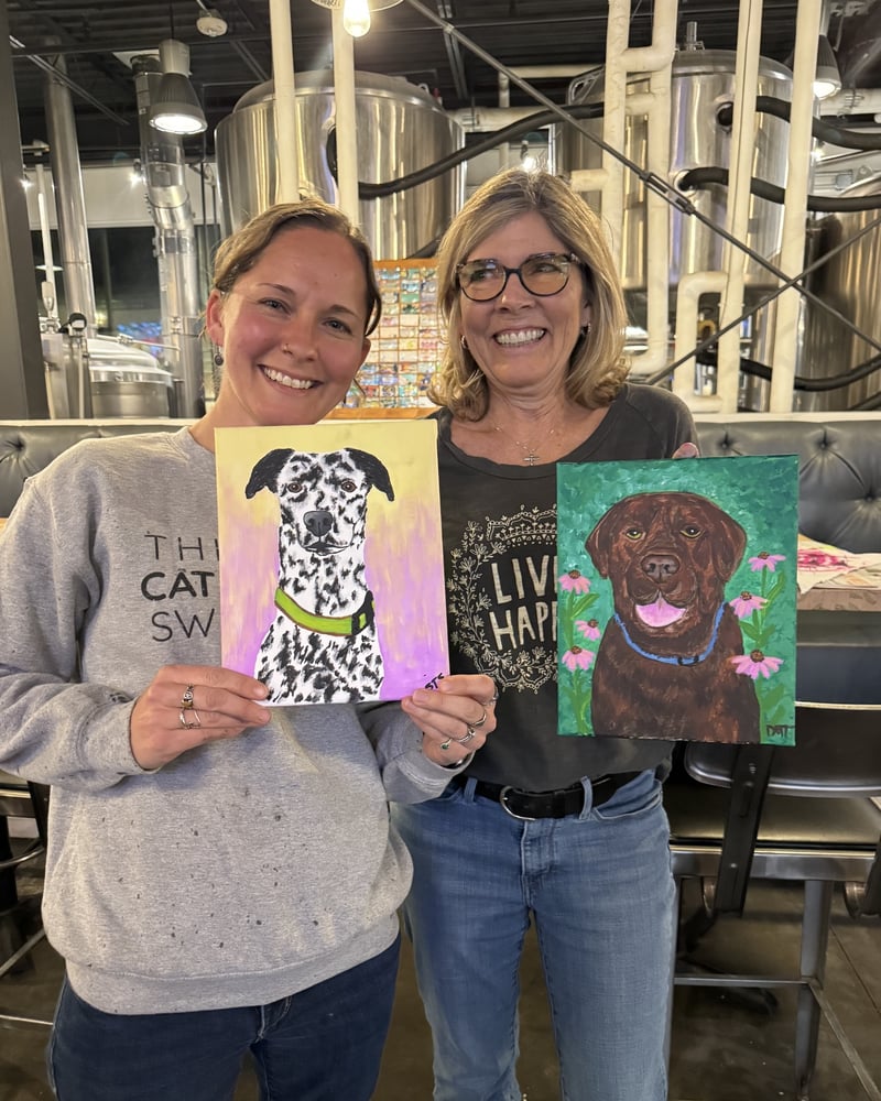 Two friends holding the pet portraits they painted at an Emma Paints paint night at Wild Blue Yonder in Castle Rock