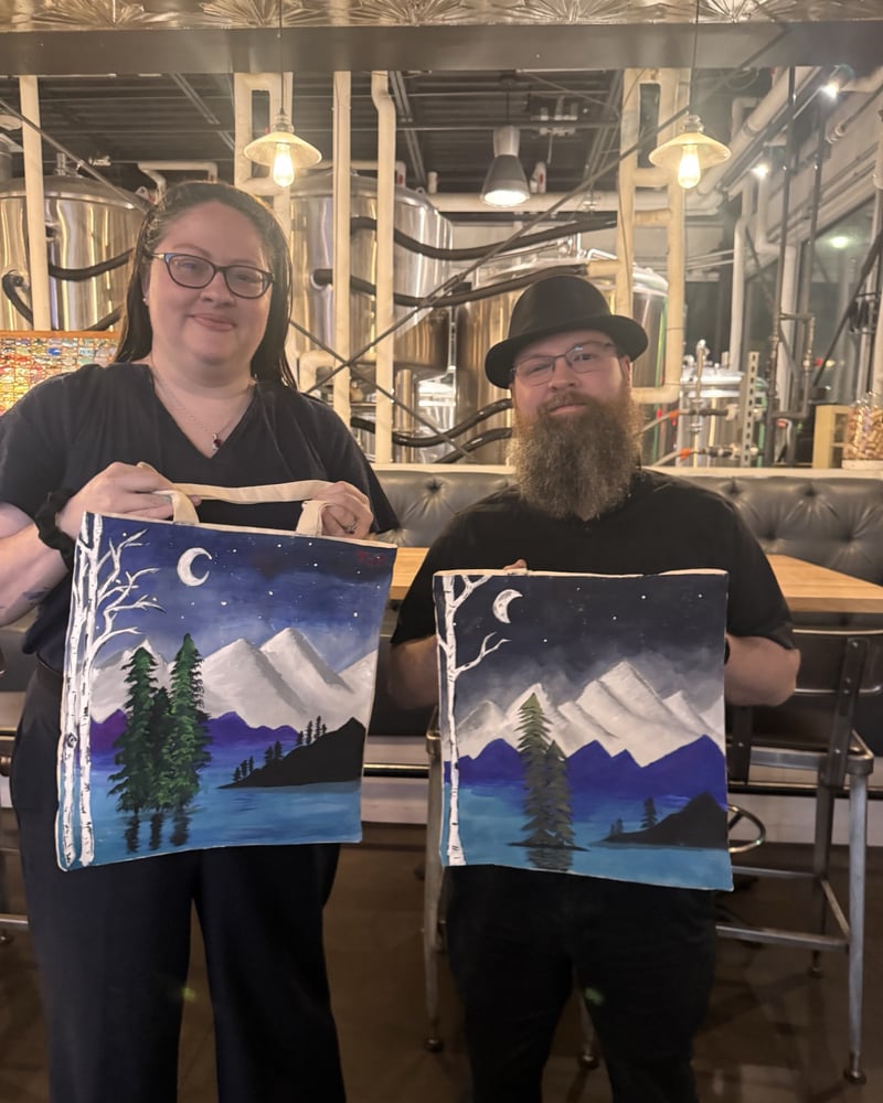 A couple holding the mountain-scene tote bags they painted at a Douglas County sip-and-paint night